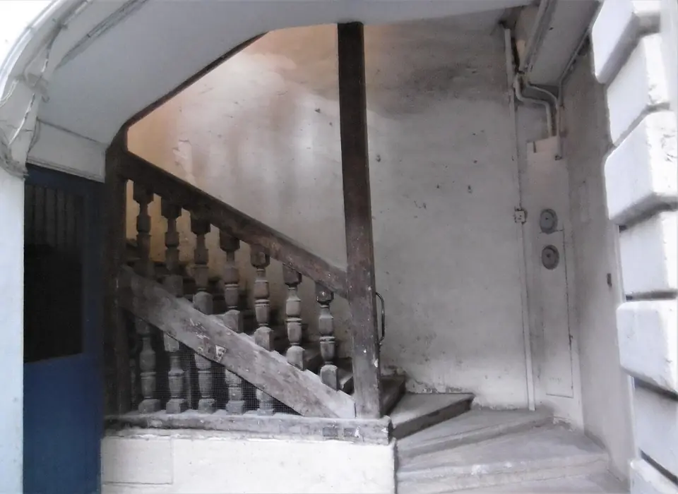 Escalier ancien du XVIIe siècle à balustres en bois tournés, dans la cage d'escalier d'un immeuble parisien aux murs clairs.